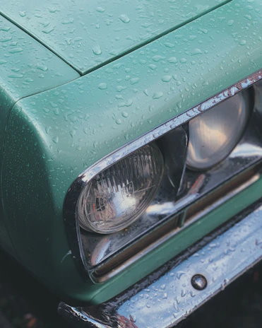 Close-up shot of a vintage car hood reflecting city lights on a rainy night.