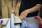 Close-up of a carpenter using a saw on a wooden plank.