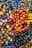 A collection of various colorful beads, some made into bracelets, with a glossy and reflective surface. The beads are arranged in a dense pile, showcasing a wide array of colors and sizes, including shades of orange, black, brown, yellow, blue, and gray.