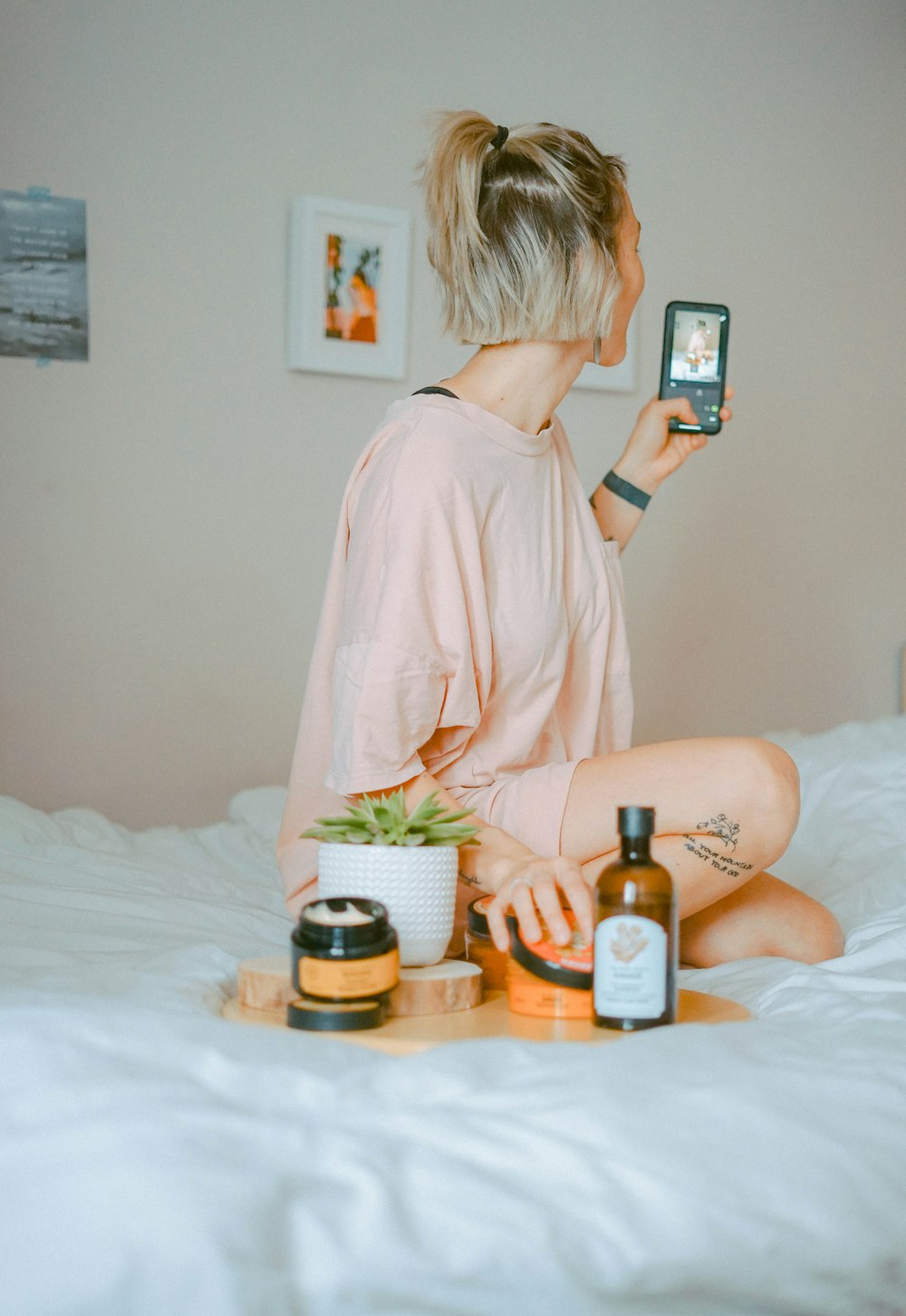 woman wearing pink shirt sitting on bed taking selfie