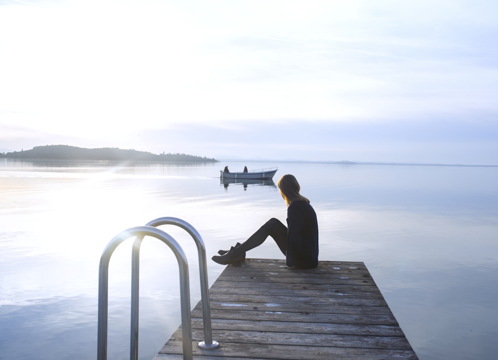 woman sitting on wooden dock near boat