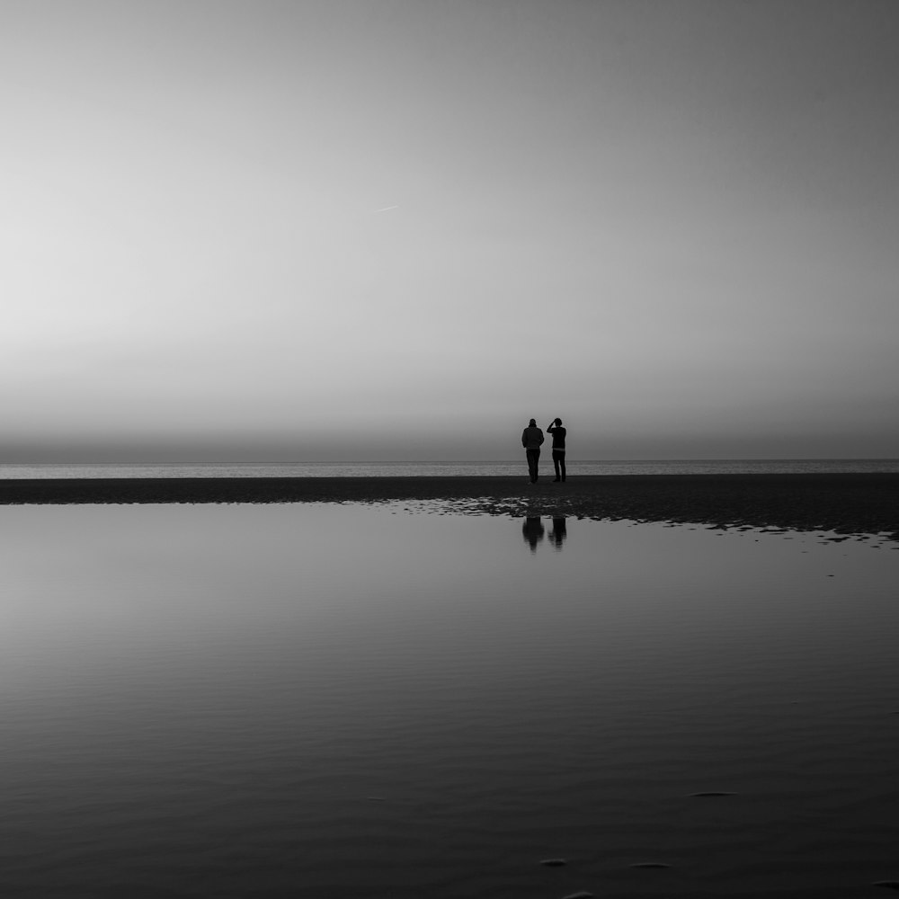 silhouette of two person standing beside calm water