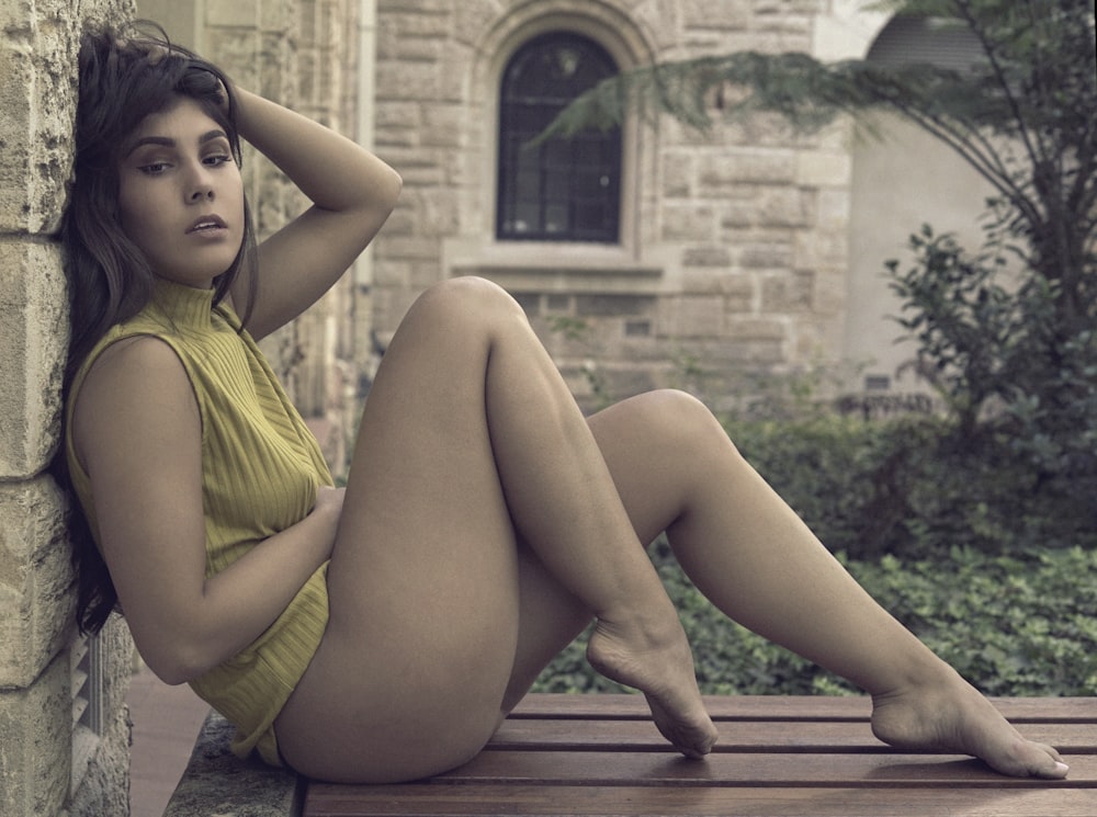 woman wearing yellow sleeveless blouse leaning on wall and sitting on wooden chair