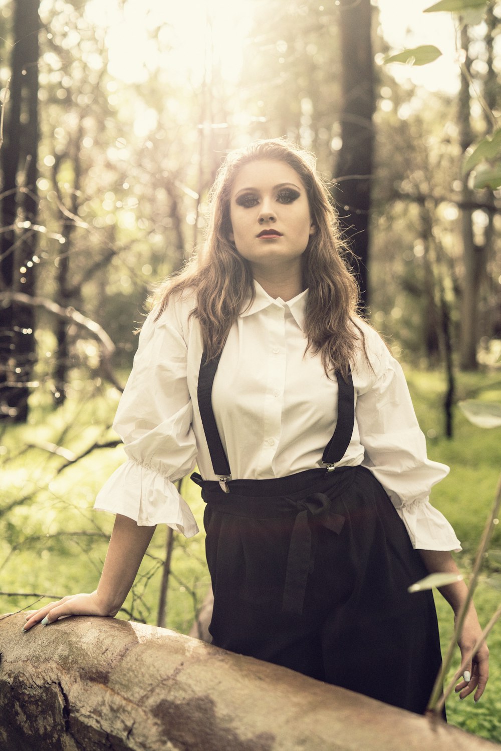 woman in white button-up long-sleeved shirt standing near fallen tree