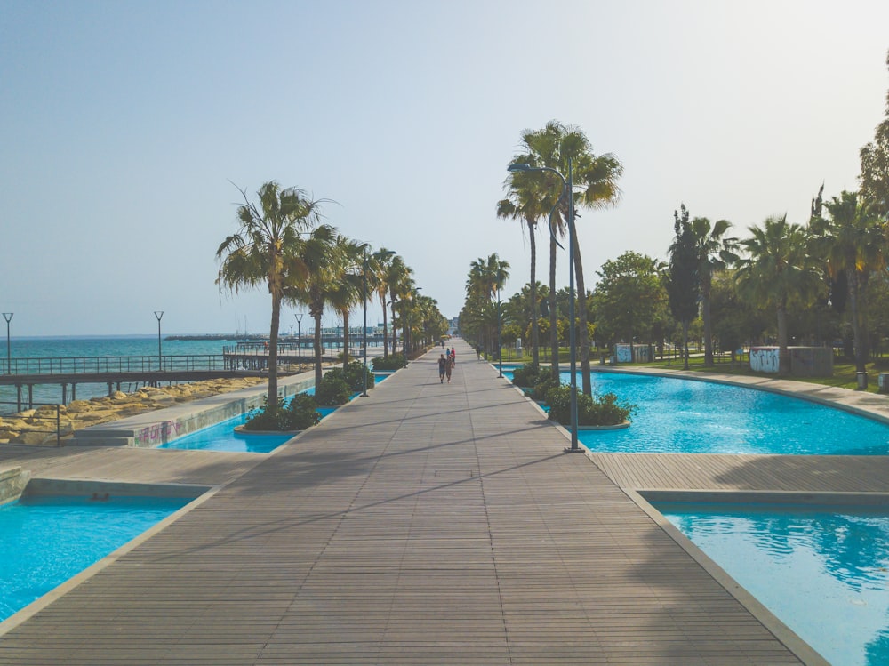 two people walking on pathway in between swimming pools