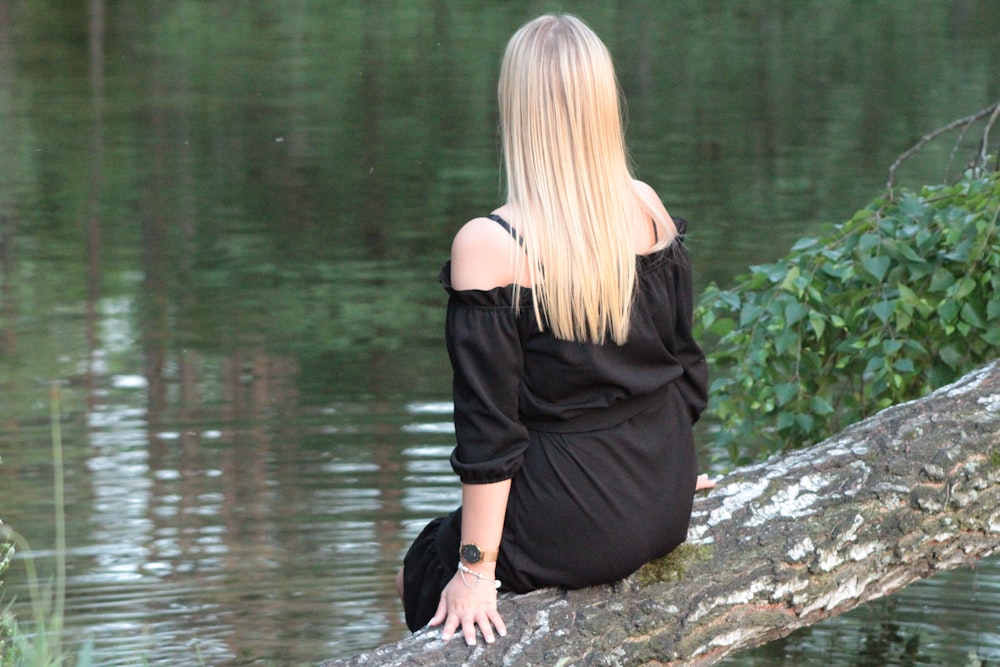 blonde woman win black off-shoulder dress sitting on log in lake shore