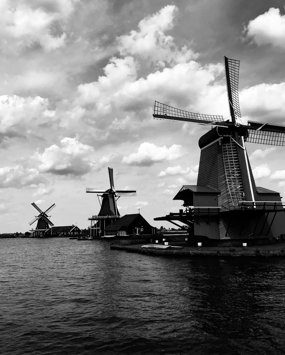 gray scale photography of windmills beside body of water