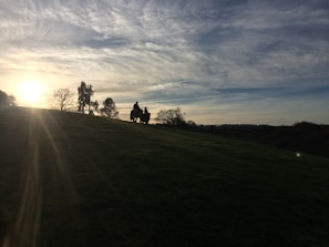 A cinematic shot of a sprawling mountain ranch at sunset, with a rider silhouetted against the glowing sky.