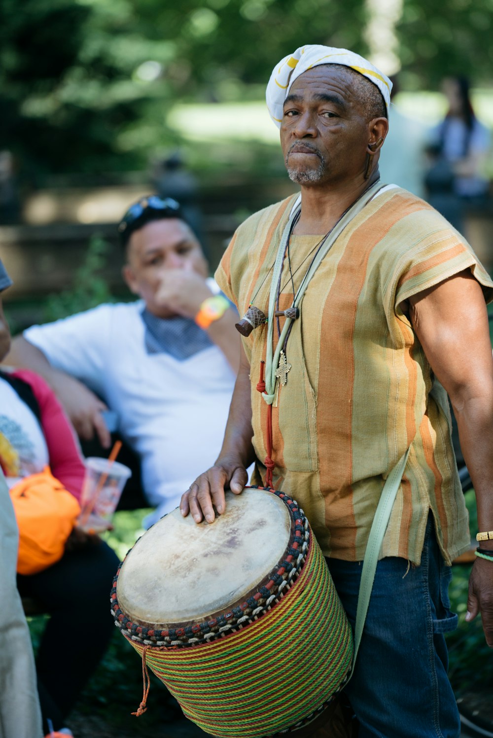 man in multicolored striped sleeveless shirt with hand drum