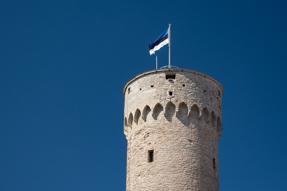 위에 파란색, 검은색 및 흰색 깃발이 있는 갈색 콘크리트 타워