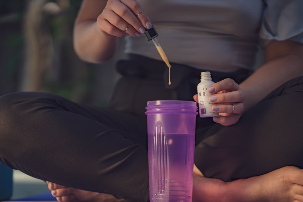 sitting woman dropping liquid using dropper on purple cup with water