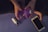 A person is sitting cross-legged on a yoga mat, holding a purple container with a white lid in their hands. A dropper bottle and a smartphone are placed next to them on the mat.