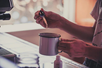 A kitchen scene showing a person adding meeminook stevia drops to their morning coffee.