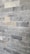 A wall composed of rectangular stone tiles with varying shades of gray and some beige accents. The surface has a rough, textured appearance with visible patterns and marks characteristic of natural stone.