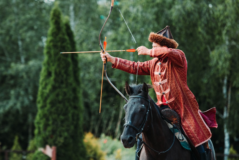 unknown person riding on black horse holding brown compound bow