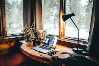 A cozy workspace with a laptop, camera, and a cup of coffee by a window overlooking a forest.
