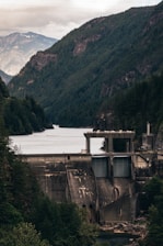 A sleek dam structure nestled in a misty mountain valley at dawn.