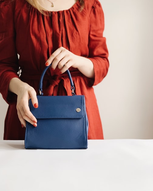 A woman holding a structured leather crossbody bag, demonstrating the elegant carry of a chain-strap design in a European urban context.