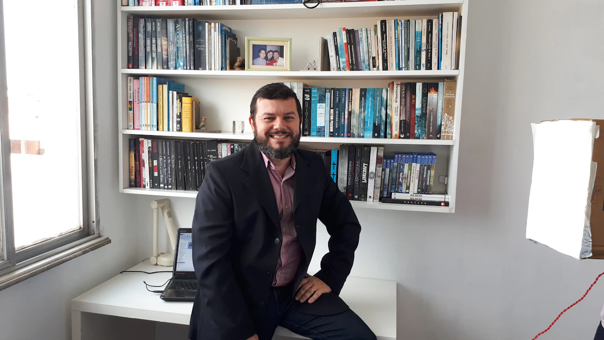 Dan Merson smiling warmly in a cozy office filled with books and research materials.