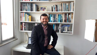 Dan Merson smiling warmly in a cozy office filled with books and research materials.
