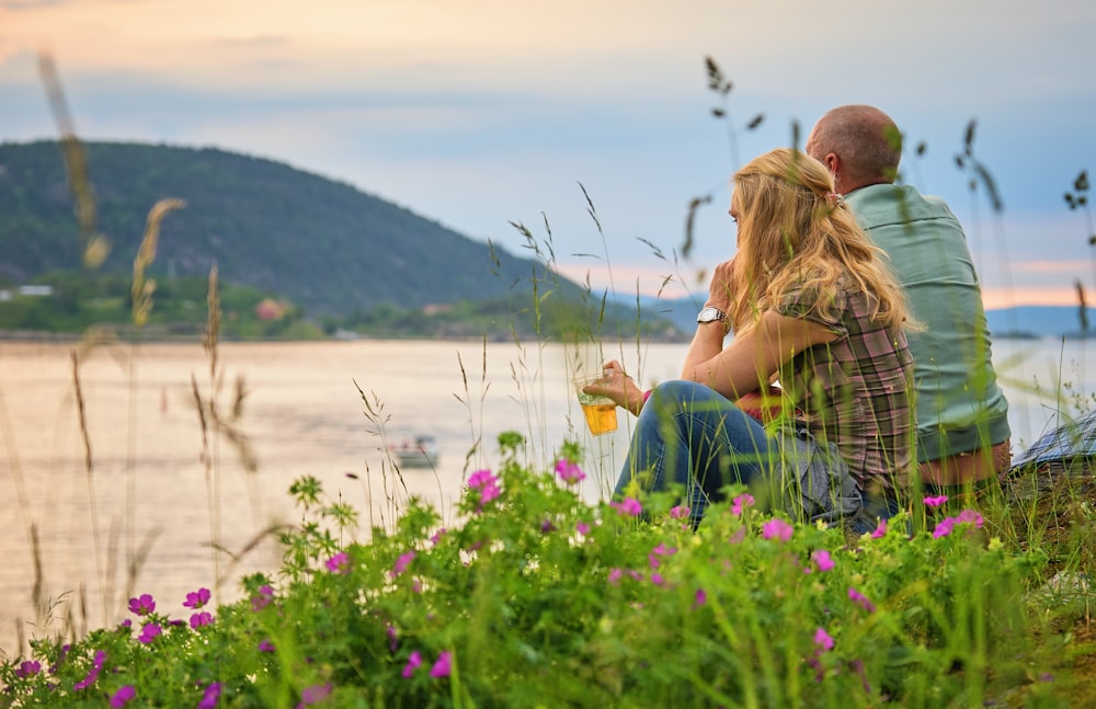 Mann und Frau sitzen tagsüber auf dem Berg mit Blick auf ein Gewässer