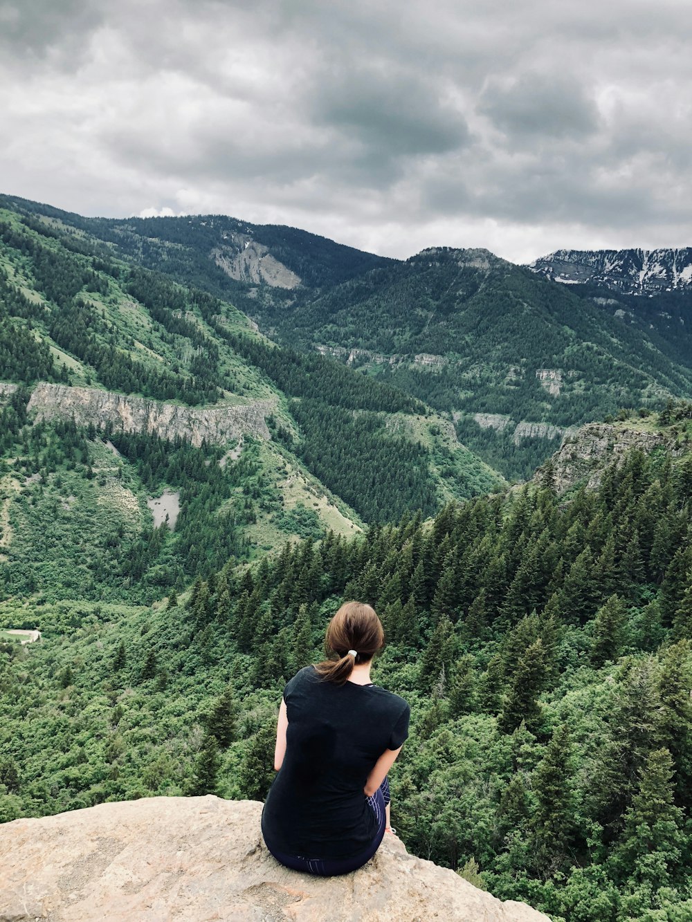 woman sitting on brown rock formation in front of mountain range during daytime