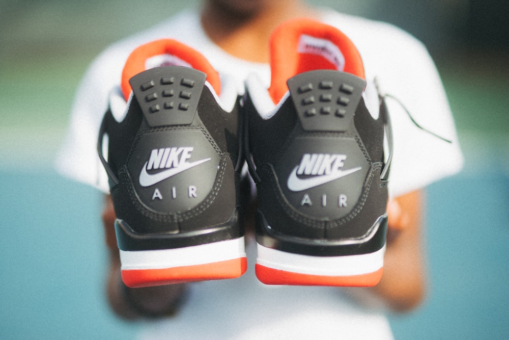 boy holding pair of black-and-orange Nike Air shoes