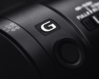 Close-up of a camera lens with a focus on the G symbol and detailed numeric markings. The image emphasizes the texture and precision of the lens design.