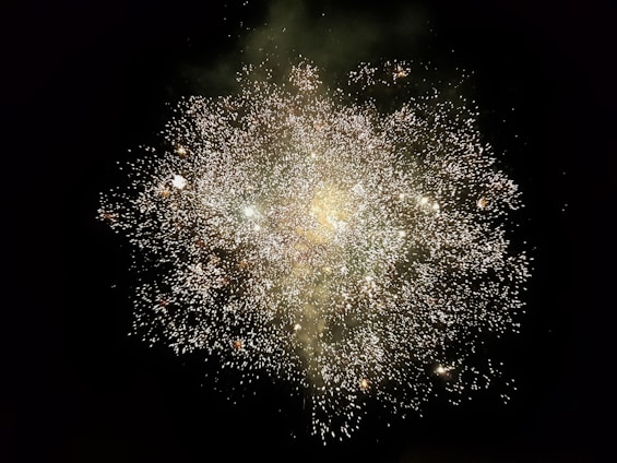 A dazzling burst of neon green and metallic gold fireworks lighting up a dark sky with smoky trails and sparks.