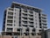 A modern multi-story building under construction with several floors featuring large windows and balconies. Workers and ladders are visible at the ground level, indicating ongoing construction or maintenance work. The architecture includes clean lines and a mix of concrete and glass materials.