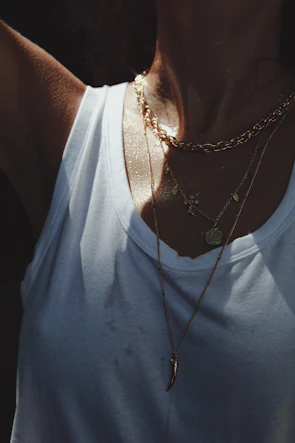 Model wearing layered gold necklaces paired with a crisp white shirt in natural daylight.