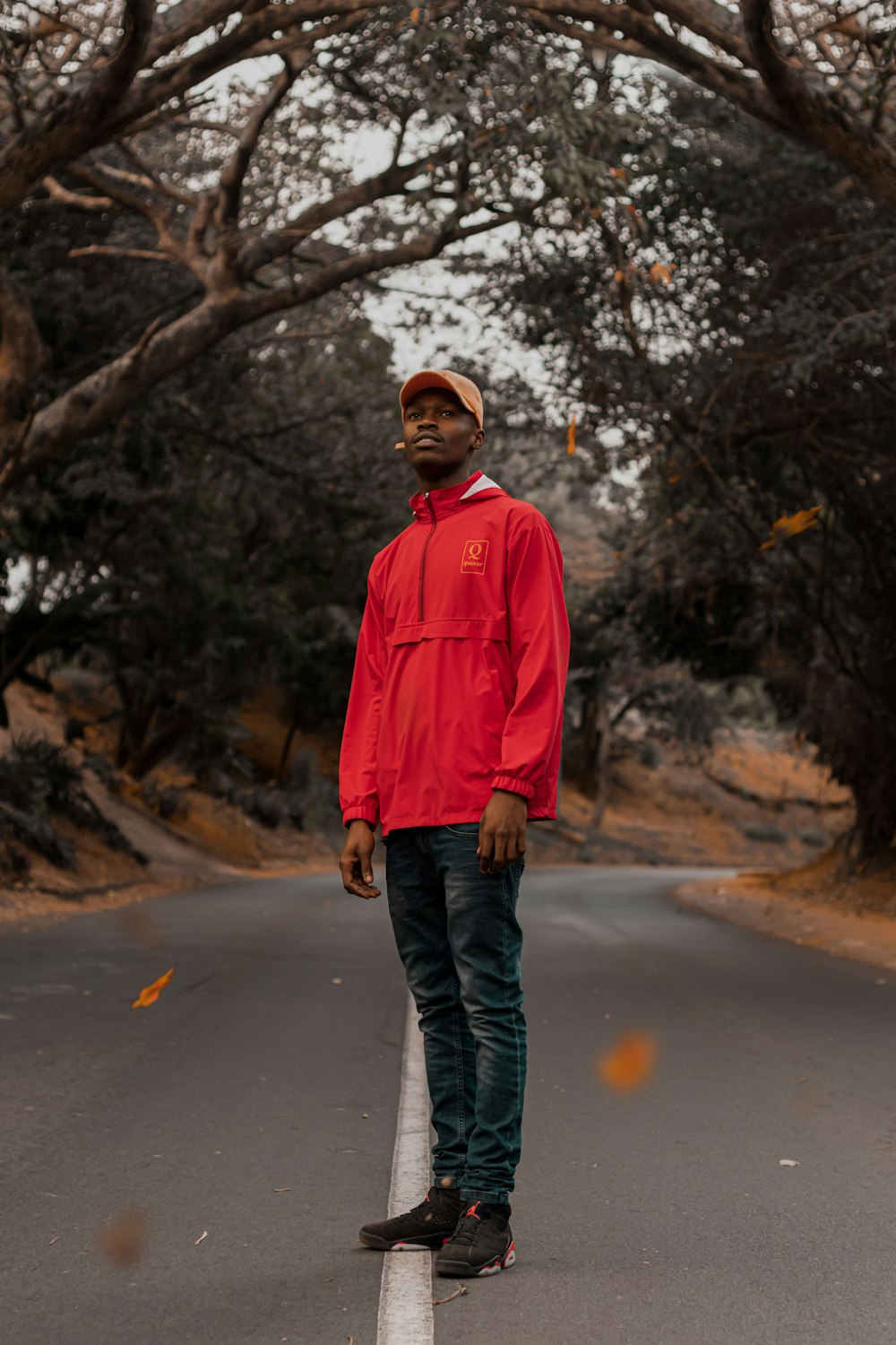 man standing on paved road under trees