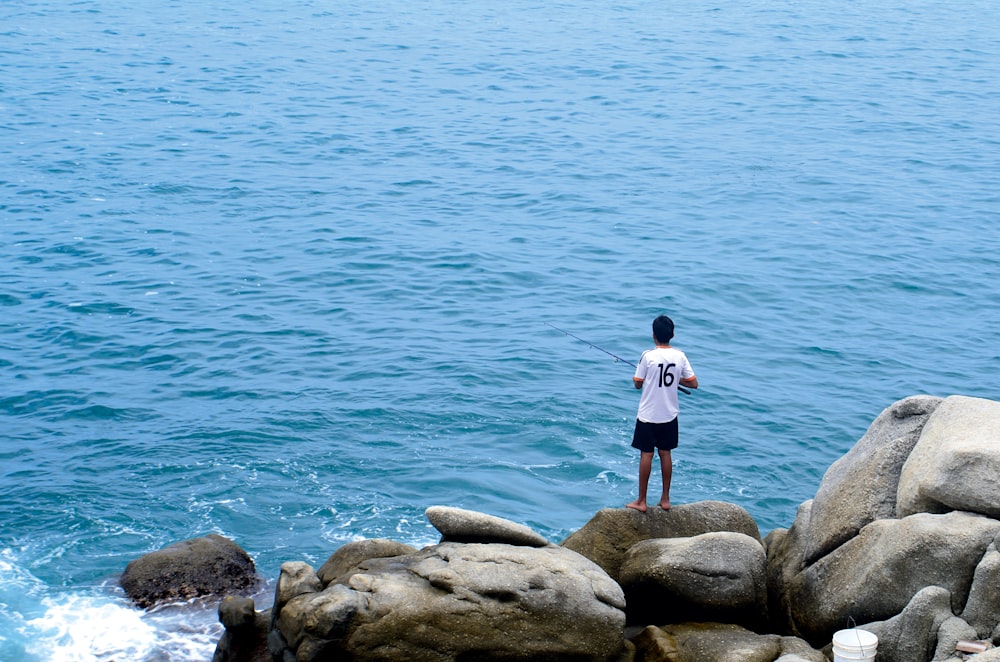 海の前の灰色の岩の上に立つ男