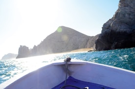 The photo captures a boat navigating through turquoise waters with rocky cliffs in the background. Sunlight brightly illuminates the scene, creating a vibrant contrast between the sea and the sky.