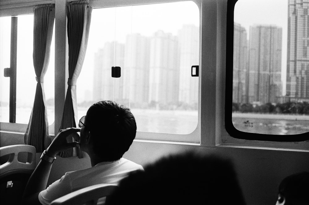 grayscale photo of man sitting beside window