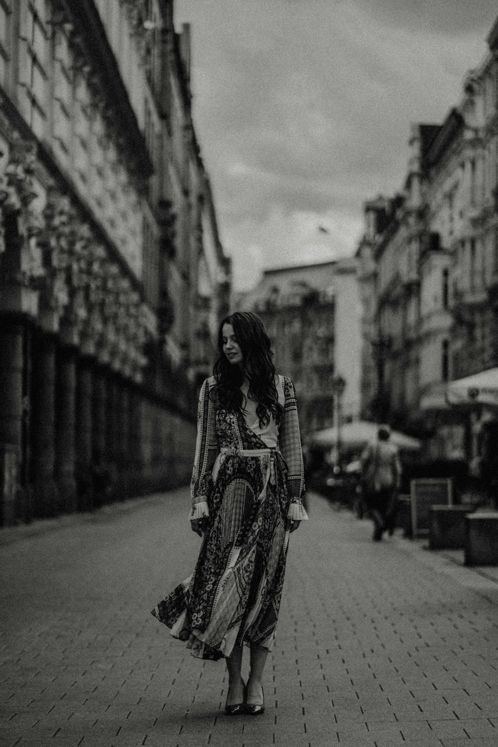 grayscale photo of woman standing on brick pavement