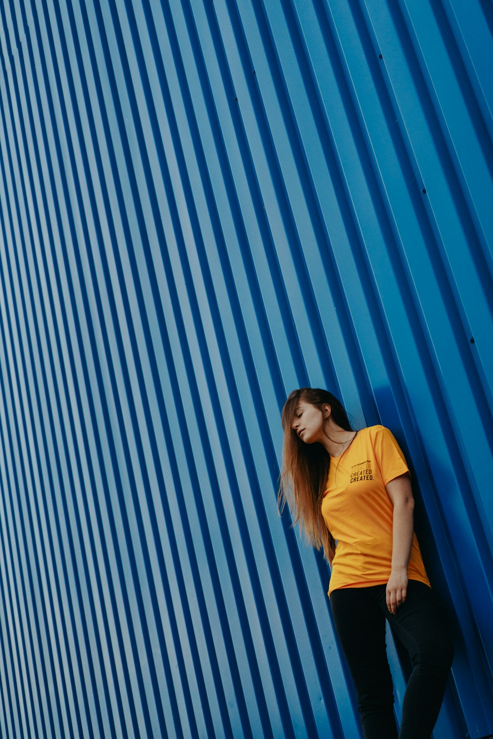 woman wearing yellow shirt leaning on blue wall