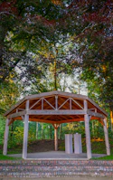 A modern gazebo with sleek design standing on a wooden deck surrounded by greenery.