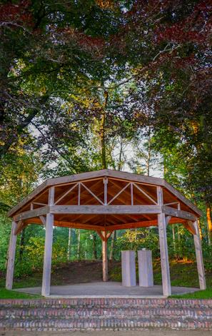 A modern gazebo with sleek design standing on a wooden deck surrounded by greenery.