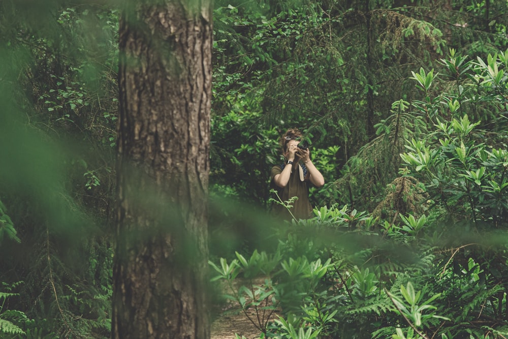 woman in green dress taking picture in the woods