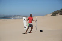 Close-up of a sandboard resting on golden beach sand with ocean waves in the background.