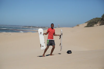 Close-up of a sandboard resting on golden beach sand with ocean waves in the background.