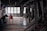 A dimly lit industrial interior with large windows on one side and various metal structures and equipment placed throughout the space. The room has a utilitarian design, featuring exposed beams and a stark ambiance. There is a long red metal conveyor table centered in the image and multiple angled chutes lined along one wall.