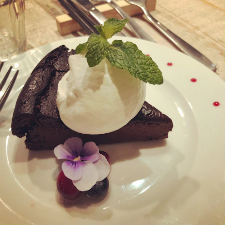 A decadent slice of chocolate cake with glossy ganache and a fresh berry garnish on a ceramic plate.