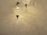 Two ornate pendant lights with a geometric lattice design, casting intricate patterns on the ceiling and wall. The lights have a warm, golden glow and are embellished with small hanging crystals.