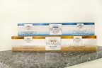Two rectangular packages of Pharma Hemp products are placed on a granite surface. The top box is labeled as 'All Natural Hemp Oil' with 850mg indicated, in a blue and white color scheme. The bottom box is labeled 'Pharma Hemp Complex' with 2500mg, featuring a gold and white color scheme. Both packages include text detailing their approximate weight and percentage.