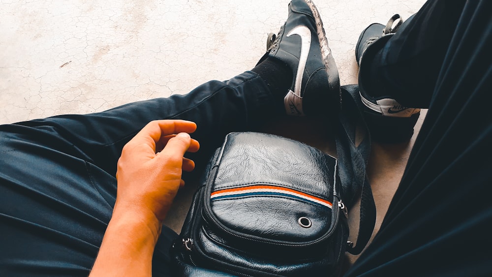 man in blue pants and pair of black and white Nike sneakers with black leather crossbody bag