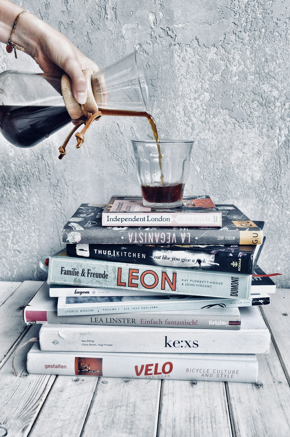 person pouring liquid on drinking glass on top of piled books