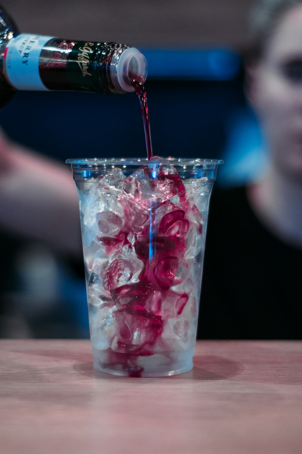 person pouring drink into clear pint glass with ice cubes