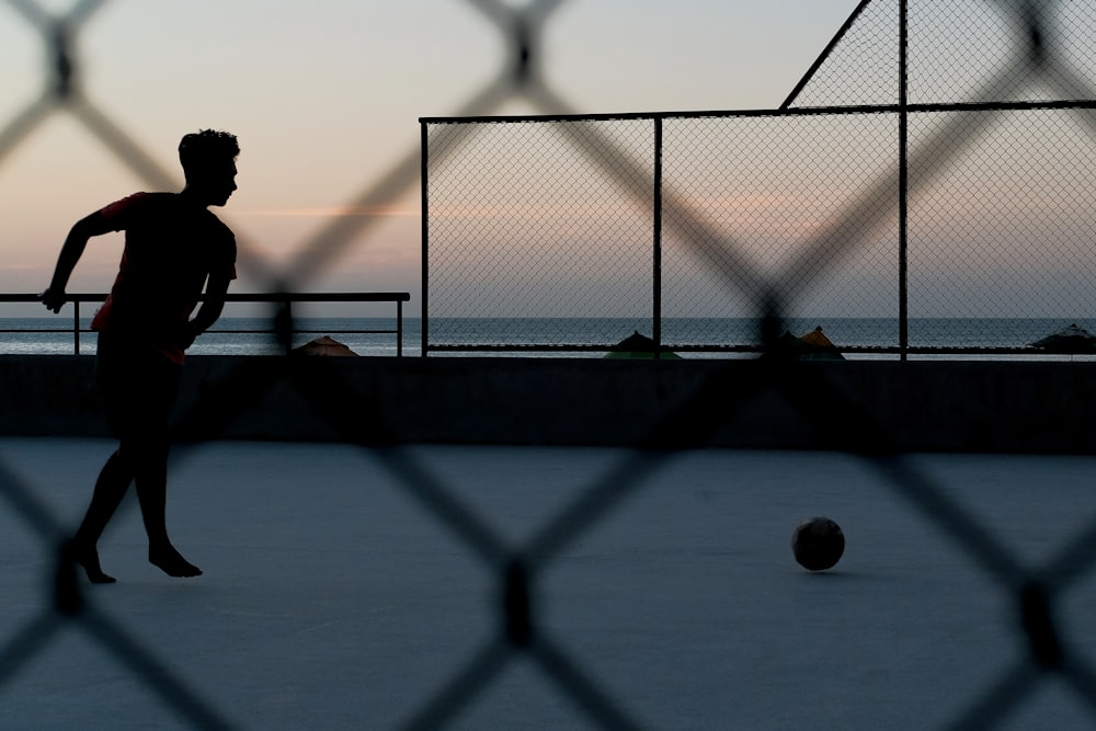 silhouette of person by ball near sea during golden hour
